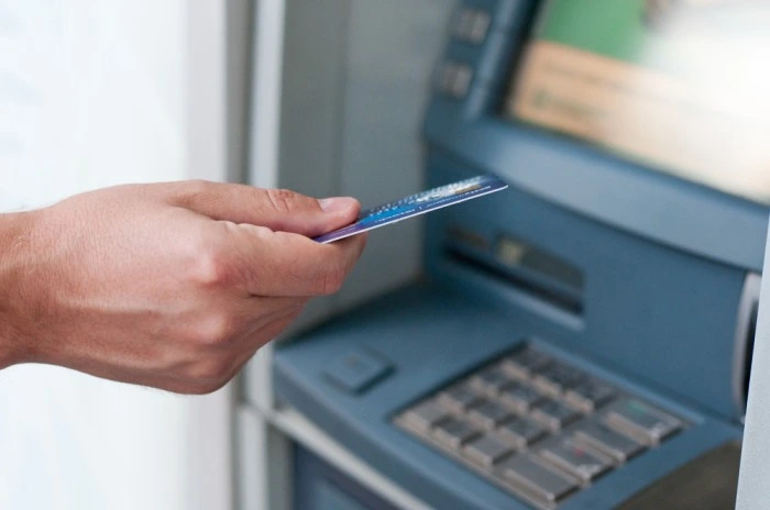 Hand inserting a debit card into an ATM machine, representing secure and convenient ATM cash withdrawal services offered by Ashoka Computer's Mini Banking solutions.