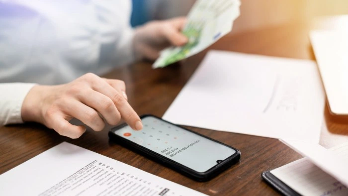 Person using a smartphone calculator while holding cash, symbolizing easy and efficient loan repayment services offered by Ashoka Computer's Mini Banking solutions.