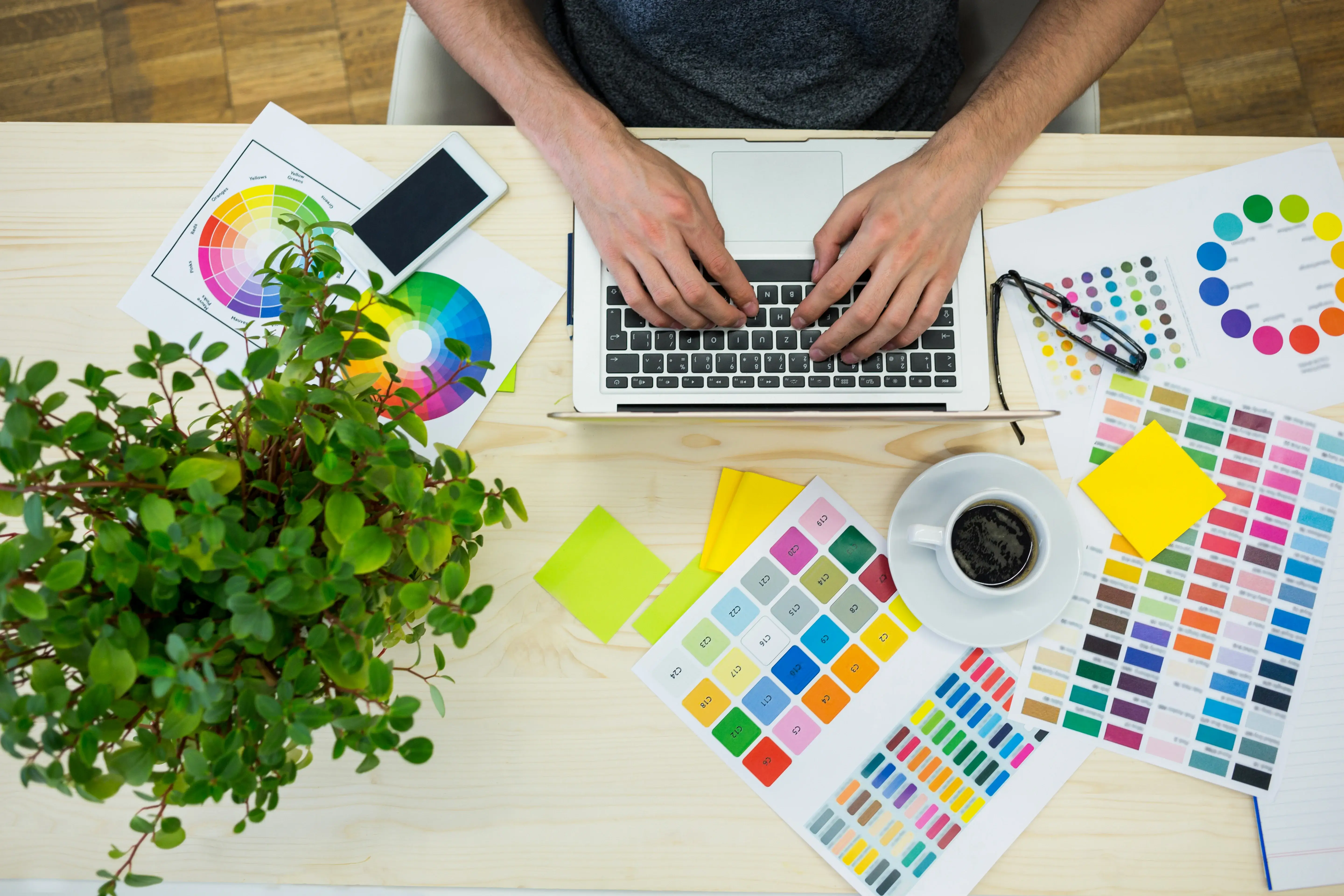 Graphic designer working on a laptop, creating vibrant offset printing designs, surrounded by color palettes and tools.
